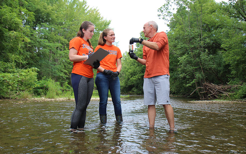 Professor Charles Driscoll in a river with two student researchers
