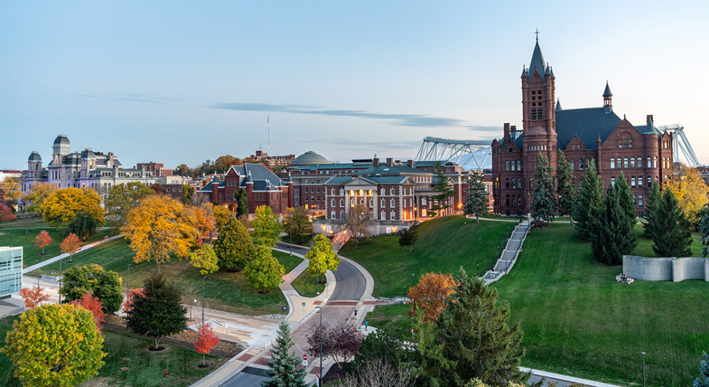 Photo of Syracuse University Campus in the Fall. The photo is from a rooftop or from the ground showing campus building and grounds in peak Central New York fall colors. this is a photo from the roof of Crouse Hinds Hall looking south east towards Crouse College Maxwell Hall and Hall of Languages at dusk.