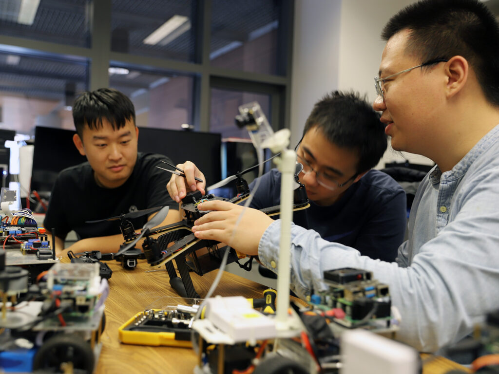 Three engineering and computer science students working in a lab on autonomous vehicle components