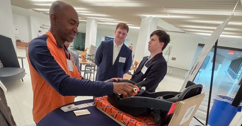 Steve Harvey stand with two students in the lobby of Link Hall examining a car seat.