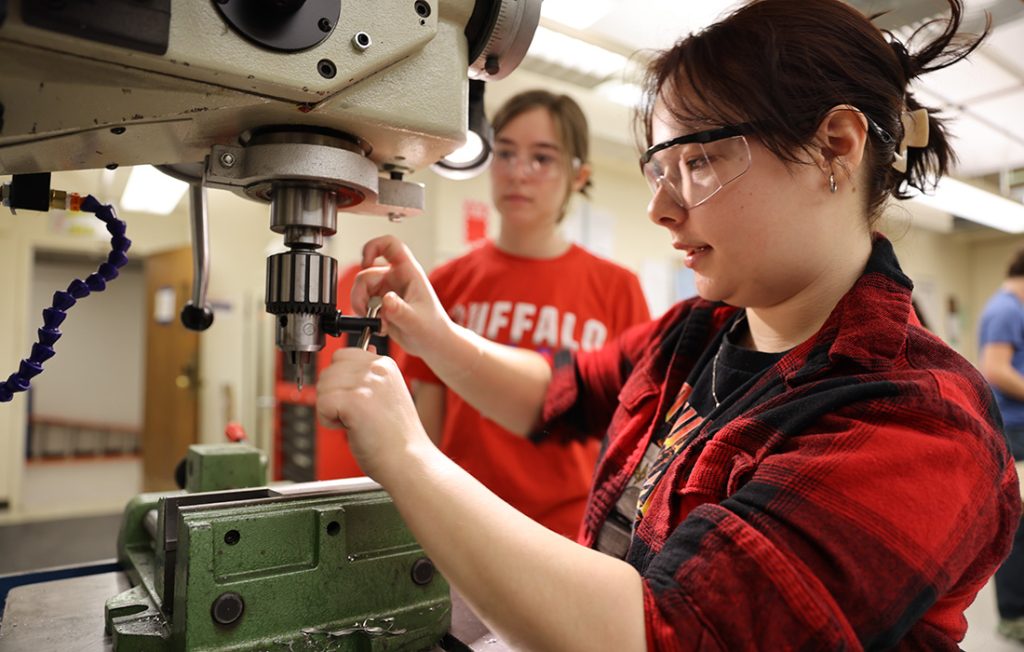 Students using a drill press to machine parts for their air engine project