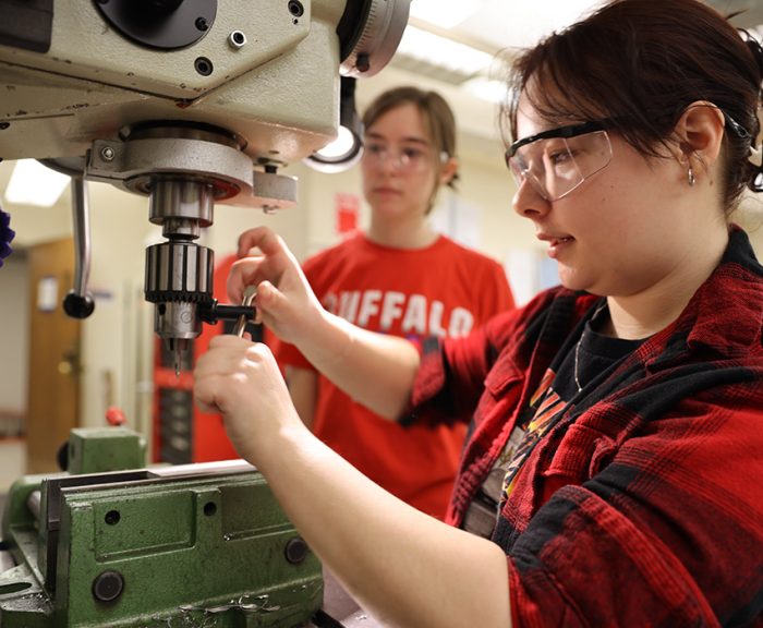 Students using a drill press to machine parts for their air engine project